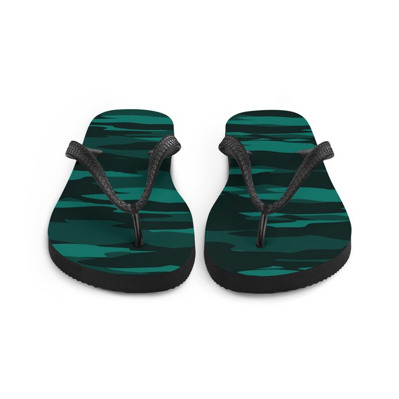 Może przedstawiać: Para klapek z wzorem kamuflażu w odcieniach turkusu i ciemnej zieleni. Paski są czarne, a podeszwy czarne. Te sandały są przeznaczone do noszenia na co dzień.