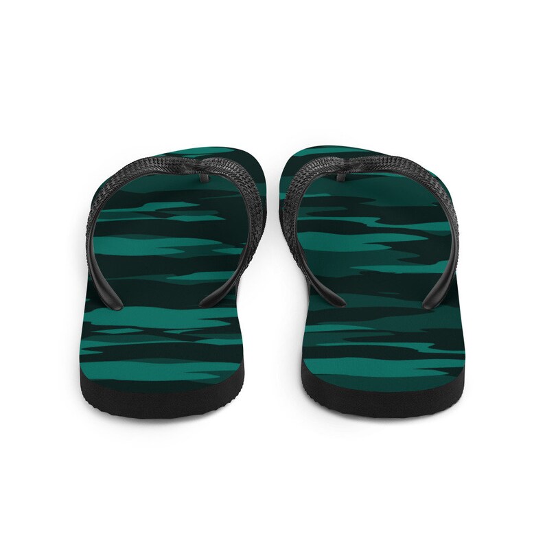 Może przedstawiać: Para klapek z wzorem kamuflażu w kolorze morskim i ciemnozielonym. Paski i podeszwy są czarne. Te klapki są przeznaczone do noszenia na co dzień, idealne na plażę lub do codziennego użytku.