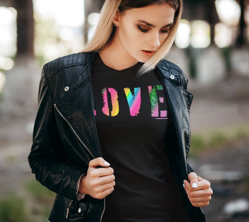 Puede incluir: Camiseta negra con la palabra "LOVE" en un dise&ntilde;o colorido y desgastado de arco&iacute;ris. La persona lleva una chaqueta de cuero negra.