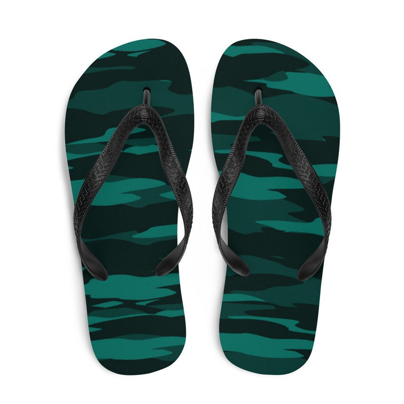 Może przedstawiać: Para klapek z ciemnozielonym wzorem kamuflażu. Paski są czarne. Te klapki są odpowiednie do noszenia na co dzień i aktywności na świeżym powietrzu.