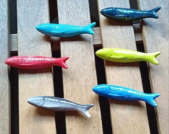 May include: Six ceramic fish figurines in various colors, including red, blue, green, and gray. The fish are arranged in a row on a wooden surface.