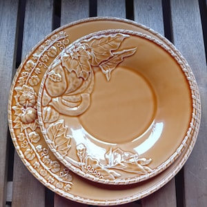 Peut inclure: Deux assiettes en céramique brunes avec un motif en relief de feuilles et de courges. Les assiettes sont imbriquées l'une dans l'autre.