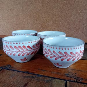 Op de afbeelding: Vier witte keramische kommen met een rood bladerenpatroon en zilveren randen staan op een houten oppervlak. De kommen hebben een afgeronde vorm en een decoratief ontwerp.