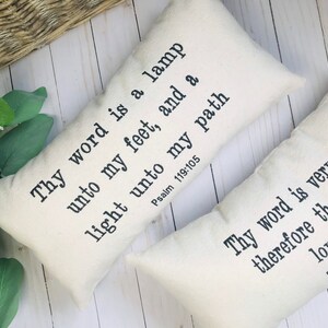 Puede incluir: Dos almohadas rectangulares decorativas de color blanquecino con texto negro. Una almohada dice: "L&aacute;mpara es a mis pies tu palabra, y lumbrera a mi camino Salmo 119:105". La otra dice: "Mucho es tu palabra amada de tu siervo Salmo 119:140."
