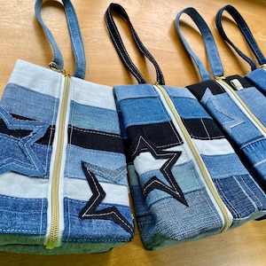 Puede incluir: Una colección de bolsos tote de mezclilla con aplicaciones de estrellas. Cada bolso presenta un diseño de patchwork de varios tonos de mezclilla azul, negro y blanco. Tienen cremalleras doradas y asas de mezclilla a juego.