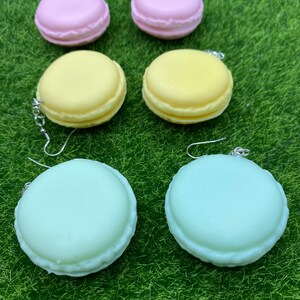May include: A set of six macaron-shaped earrings in pink, yellow, and green. The earrings are made of polymer clay and have a glossy finish.