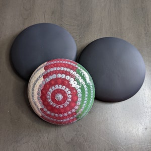 May include: Three round stones, two painted black and one painted with a red, white, and green mandala design.
