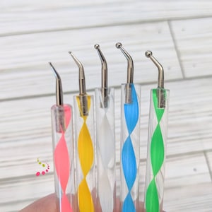 May include: Five nail art tools with different colored swirl designs. The tools have a silver metal tip and a clear plastic handle.