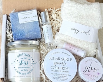 May include: A gift box containing a blue handcrafted soap, a glass jar candle with the text Good Friends are like stars, a rollerball body oil, white fuzzy socks, a strawberry sorbet lip balm, a round sugar scrub tin, and a small glow lotion tin.