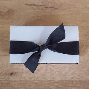 May include: A white gift box with a black satin ribbon tied in a bow.