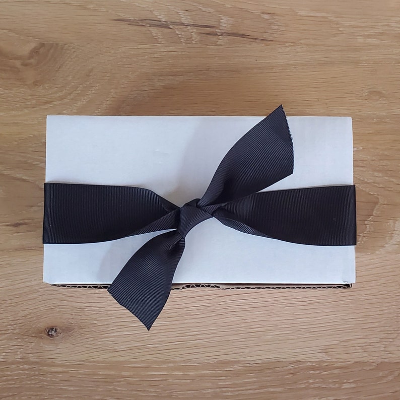 May include: A white gift box with a black satin ribbon tied in a bow.