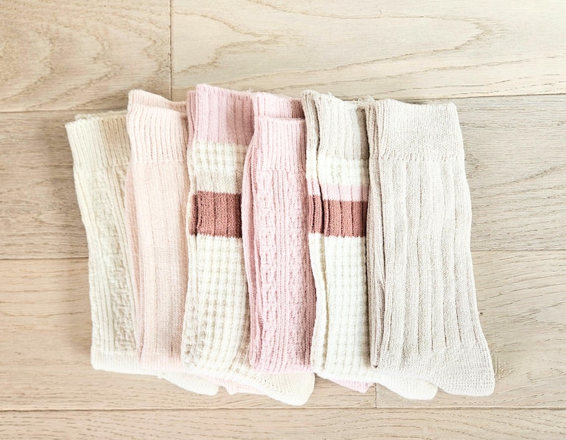 May include: A stack of six pairs of socks in various shades of pink and beige. The socks have a ribbed texture and some have a brown stripe.