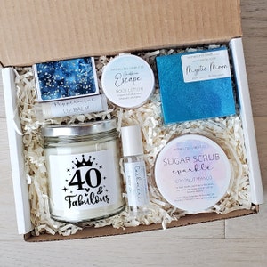May include: A gift box filled with self-care items for a 40th birthday. The box includes a candle with the text "40 & Fabulous", a sugar scrub, a bar of soap, a body lotion, and a lip balm.