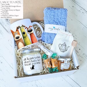 Pu&ograve; includere: Una confezione regalo con una tazza con illustrazioni di cani dei cartoni animati, una candela, calzini blu, bustine di t&egrave;, miele, burrocacao e caramelle. La candela recita "at least you don't have to wear a cone".