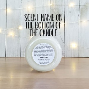 May include: White candle jar with a black label. The label says "SCENT NAME ON THE BOTTOM OF THE CANDLE". The label also includes safety instructions and the scent name "SUGAR COOKIE".