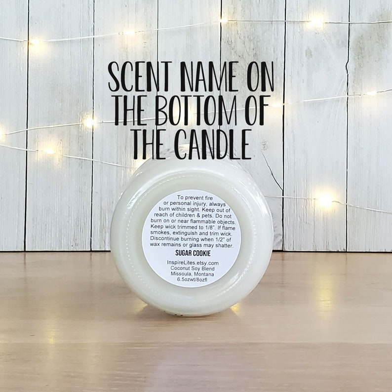 May include: White candle jar with a black label. The label says "SCENT NAME ON THE BOTTOM OF THE CANDLE". The label also includes safety instructions and the scent name "SUGAR COOKIE".