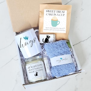 Pu&ograve; includere: Confezione regalo con una tazza bianca con la scritta "hugs", una candela, preparato per torte, calzini blu e balsamo per le labbra. La candela dice "at least you don't have to wear a cone". I calzini dicono "cozy socks".