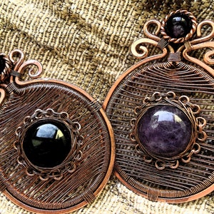 May include: Two copper wire wrapped pendants with gemstone cabochons. One pendant features a black gemstone and the other features a purple gemstone.
