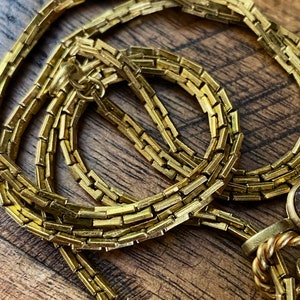 May include: A gold chain necklace with a box chain design. The chain is made of small, rectangular links.