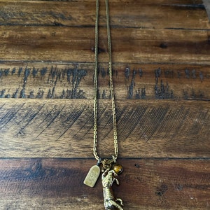 May include: A gold chain necklace with a tiger charm and a small amber bead. The tiger is holding a ball in its paws.