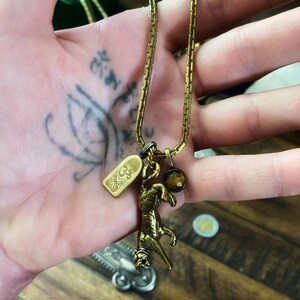 May include: A gold chain necklace with a tiger charm, a small tag with a skull and crossbones, and a brown gemstone pendant.