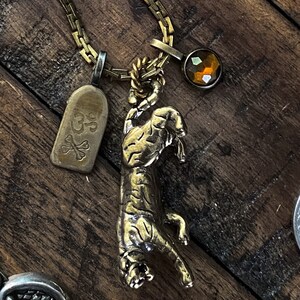 May include: A gold chain necklace with a tiger pendant, a small tag with the text "GP" and a crossbones design, and a brown faceted gemstone.