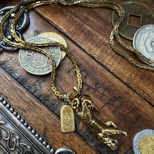 May include: A gold chain necklace with a tiger pendant and a small charm with the symbol "Om" on it. The necklace is lying on a wooden surface with several coins.