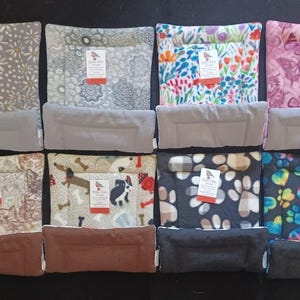 May include: A collection of pet beds with various patterned designs, including floral, butterfly, and paw prints. Each bed has a rectangular shape with a soft, cushioned interior and a raised bolster. The beds come in a variety of colors.