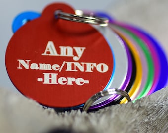 May include: A stack of colorful, round pet tags with a silver ring. The front tag is red with the text "Any Name/INFO -Here-" in white. Other tags are blue, silver, purple, green, and yellow.