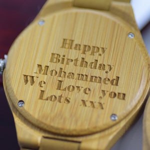 May include: Close-up of a wooden watch with the engraved message "Happy Birthday Mohammed We Love you Lots xxx". The watch has a light brown color and a silver crown. The watch is a personalized gift.