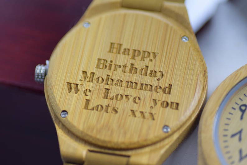 May include: Close-up of a wooden watch with the engraved message "Happy Birthday Mohammed We Love you Lots xxx". The watch has a light brown color and a silver crown. The watch is a personalized gift.