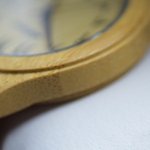 May include: Close-up of a bamboo watch. The watch has a light brown wooden frame and a light-colored watch face. The watch band is also made of bamboo. The watch is a natural, eco-friendly accessory.