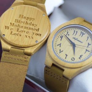 May include: Two bamboo watches with leather straps. One watch has Arabic numerals and the brand name "shifenmei" on the face. The other watch has the inscription "Happy Birthday Mohammed We Love you Lots xxx" engraved on the back.
