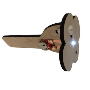 May include: A wooden, light-coloured, decorative object with a black outline, resembling a flower or a clover. It has a small light and some copper-coloured electrical components. The object has a flat, angled base.