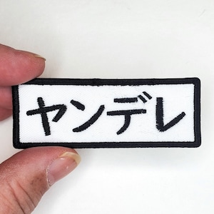 Puede incluir: Parche blanco bordado con contorno negro y el texto japonés "Yankee" en negro.