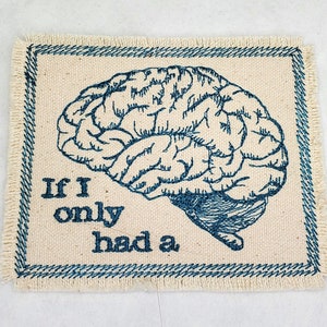 May include: A beige fabric patch with blue embroidery. The patch features a stylized drawing of a brain and the text "If I only had a."