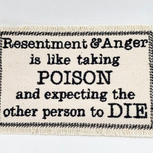May include: A white fabric patch with black embroidered text that reads "Resentment & Anger is like taking POISON and expecting the other person to DIE."
