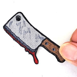 May include: A gray embroidered iron-on patch of a bloody butcher knife with a brown handle.