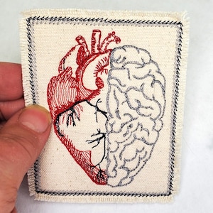 May include: A white fabric patch with a red embroidered heart and a gray embroidered brain. The heart and brain are intertwined.