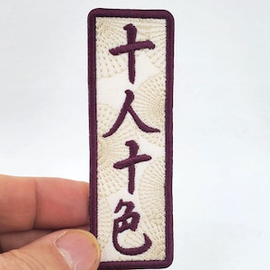 Puede incluir: Un parche bordado blanco con un borde burdeos. El parche presenta caracteres japoneses que se leen "Tenjin", que es el nombre de un santuario sintoísta en Japón.