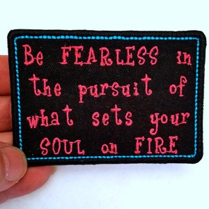 May include: Black embroidered patch with blue stitching around the edges. The text reads "Be FEARLESS in the pursuit of what sets your SOUL on FIRE" in pink thread.