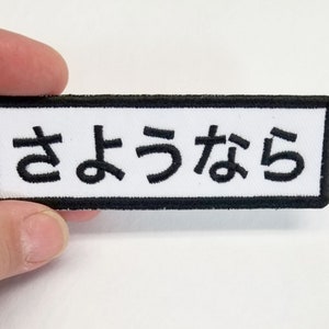 May include: White embroidered patch with black border and the Japanese text "さよなら" (sayonara) meaning "goodbye".