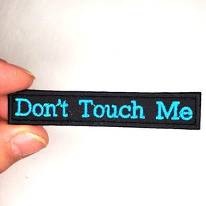 May include: Black embroidered patch with the text "Don't Touch Me" in turquoise blue.