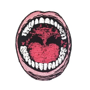 Puede incluir: Un parche bordado que representa una boca abierta de par en par con dientes blancos, en rosa y negro.