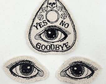 Puede incluir: Tres parches bordados con un ojo blanco y negro con una calavera negra y las palabras "YES NO GOODBYE" sobre un fondo blanco.