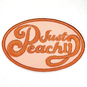 May include: Orange embroidered patch with the text "Just Peachy" on a light pink background.