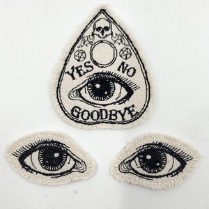 May include: Three embroidered patches featuring a black and white eye with a black skull and the words "YES NO GOODBYE" on a white background.