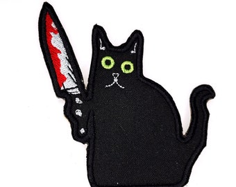 Op de afbeelding: Zwarte kat met groene ogen die een rood en wit mes vasthoudt. De kat zit op een witte achtergrond.