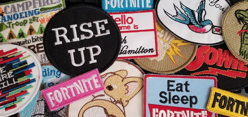 May include: A collection of embroidered patches featuring various designs and phrases, including "Rise Up", "Fortnite", "Eat Sleep", "You!" and "Bowie".