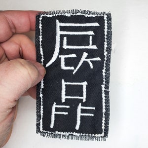 May include: Black fabric patch with white embroidered Japanese characters. The characters read "后 々 曰"